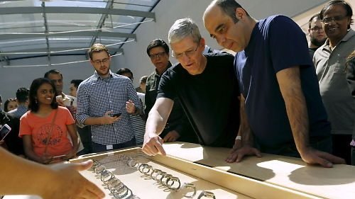 Tim Cook and Baha Cinar leaning over an Apple Watch display table inside an Apple Store, customers gathered around